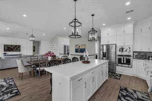 Kitchen with a breakfast bar area, stainless steel appliances, open floor plan, white cabinets, and lofted ceiling