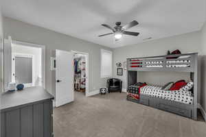 Bedroom with a walk in closet, light carpet, and a ceiling fan