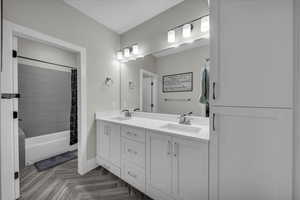 Full bathroom with double vanity, shower / bath combo with shower curtain, and parquet flooring