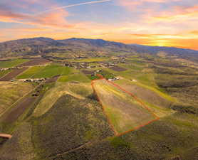 Expansive land parcel outlined in red, featuring varied terrain including open fields and sloped, brush-covered areas