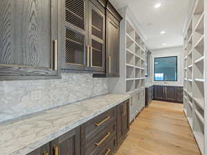 Pantry area featuring dark wood finish cabinetry, open shelves, light wood finished floors, glass insert cabinets, and light stone countertops