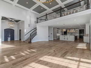 Unfurnished living room with hanging lights, coffered ceiling, ornamental molding, and light wood-style floors