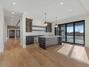Walkout kitchen with open shelves, decorative light fixtures, glass insert cabinets, light wood-style flooring, and ornamental molding