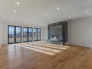 Unfurnished living room with light wood finished floors, brick wall, french doors, a fireplace, and recessed lighting