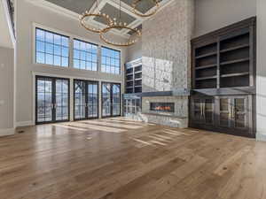 Unfurnished living room with built in features, light wood-style floors, a high ceiling, suspended lighting, and a fireplace