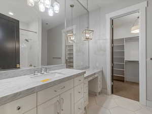 Full bath with a spacious closet, vanity, tiled shower, light tile patterned floors, and light colored carpet