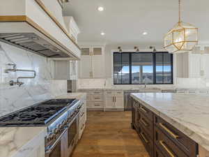 Two tone kitchen featuring light stone counters, stainless steel appliances, two tone color scheme, light wood-type flooring, and glass insert cabinets