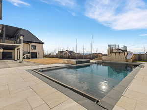 Integrated pool / hot tub featuring a patio, a water slide, a fenced backyard, and a balcony