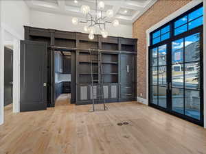 Main floor office with hidden room opened coffered ceiling, light wood-style flooring, and suspended lighting