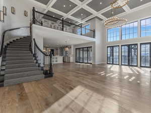 Unfurnished living room with suspended lighting, coffered ceiling, light wood finished floors, and french doors