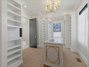 Primary bedroom walk in closet with light colored carpet and a chandelier