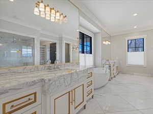 Primary bathroom featuring two vanities, a shower stall, ornamental molding, a spacious closet, and a soaking tub
