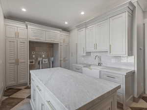 Laundry room with decorative backsplash, a kitchen island, recessed lighting, light stone counters, and white cabinets