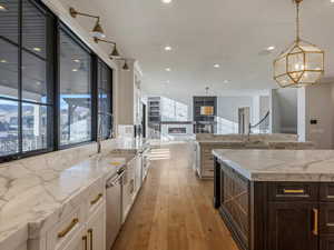 Sunset views from the kitchen with a stone fireplace, dual tone cabinets, light stone countertops, pendant lighting, and light wood finished floors