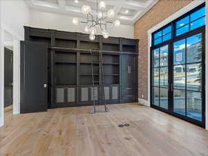 Main floor office with hidden room closed featuring coffered ceiling, suspended lighting, light wood-style floors, and brick wall