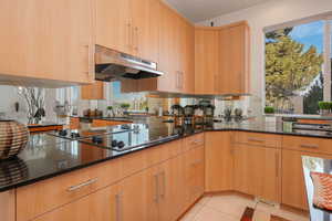Kitchen featuring dark stone countertops, light tile patterned floors, black electric cooktop, and a peninsula