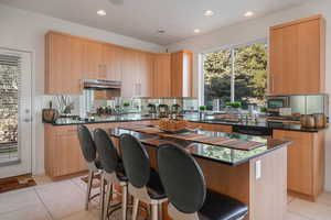 Kitchen featuring dark stone counters, recessed lighting, a breakfast bar, a center island, and light tile patterned floors