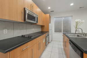 Kitchen with dark countertops, stainless steel appliances, light tile patterned floors, recessed lighting, and tasteful backsplash