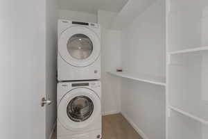 Laundry room with stacked washing machine and dryer and wood finished floors