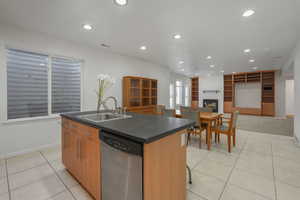 Kitchen featuring a center island with sink, dishwasher, recessed lighting, a fireplace, and light tile patterned floors