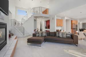 Living room with a high ceiling, light tile patterned flooring, a tiled fireplace, and recessed lighting