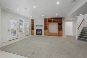 Unfurnished living room with recessed lighting, a fireplace with flush hearth, light tile patterned floors, built in shelves, and light carpet