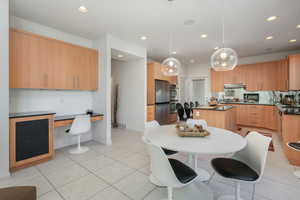 Kitchen with a center island, hanging light fixtures, stainless steel appliances, light tile patterned flooring, and built in desk