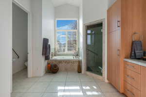 Full bath with a shower stall, a garden tub, light tile patterned floors, and lofted ceiling