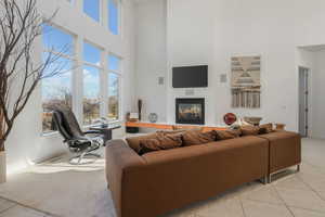 Living area with tile patterned flooring, a glass covered fireplace, and a high ceiling