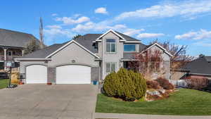 View of front of home with stucco siding, an attached garage, a front lawn, concrete driveway, and stone siding