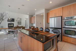Kitchen with stainless steel appliances, dark stone counters, decorative light fixtures, a glass covered fireplace, and a center island