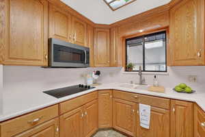 Kitchen with light countertops, stainless steel microwave, and black electric cooktop