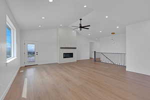 Unfurnished living room with a large fireplace, light wood-type flooring, ceiling fan, a high ceiling, and recessed lighting