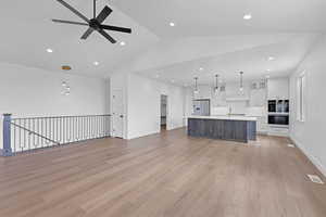 Kitchen with open floor plan, dual tone cabinetry, glass fronted cabinets, decorative light fixtures, and a large island
