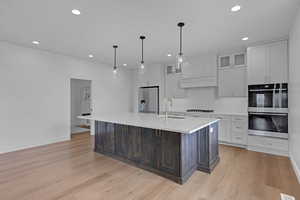 Kitchen with glass insert cabinets, stainless steel appliances, two tone color scheme, an island with sink, and hanging light fixtures