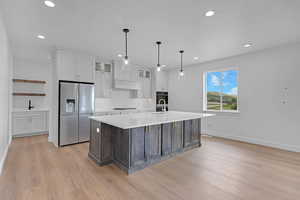 Dual tone kitchen featuring dual tone cabinetry, glass fronted cabinets, a center island with sink, stainless steel appliances, and pendant lighting