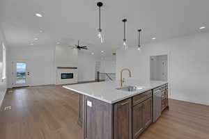 Kitchen featuring dark wood finish cabinets, a large fireplace, light wood finished floors, light stone countertops, and decorative light fixtures