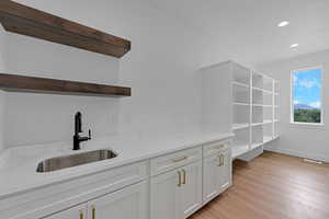 Bar area with open shelves, white cabinetry, light stone counters, light wood-type flooring, and recessed lighting