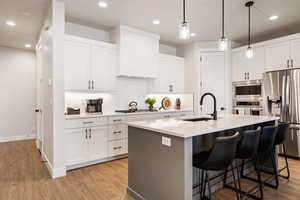 Kitchen with stainless steel appliances, light wood finished floors, an island with sink, a breakfast bar area, and hanging light fixtures
