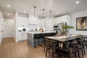 Kitchen with decorative light fixtures, white cabinetry, a kitchen breakfast bar, and light wood-type flooring