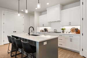 Kitchen featuring a breakfast bar area, a kitchen island with sink, decorative light fixtures, light wood-style flooring, and tasteful backsplash