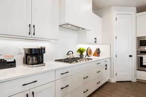 Kitchen featuring white cabinets, stainless steel appliances, dark wood-type flooring, tasteful backsplash, and light stone counters