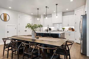 Kitchen with a center island with sink, light wood-style floors, freestanding refrigerator, decorative light fixtures, and backsplash