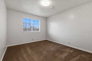 Empty room with dark colored carpet and a textured ceiling