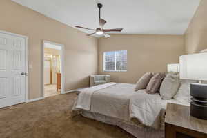 Carpeted bedroom with a ceiling fan, vaulted ceiling, and connected bathroom