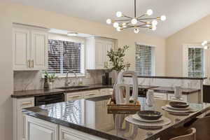 Kitchen featuring a breakfast bar area, a center island, dark stone counters, hanging lights, and black dishwasher