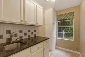 Kitchen featuring a textured ceiling, dark stone countertops, decorative backsplash, and white cabinetry