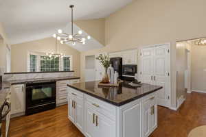 Kitchen featuring a chandelier, black appliances, white cabinetry, vaulted ceiling, and dark stone counters