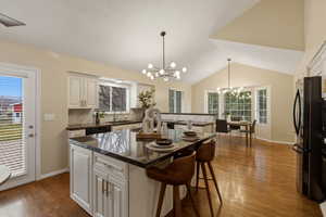 Kitchen with a breakfast bar area, black appliances, dark stone countertops, light wood finished floors, and a kitchen island