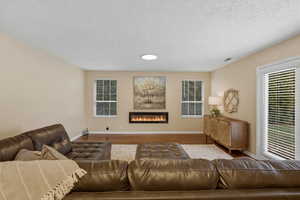 Living area featuring wood finished floors, a glass covered fireplace, and a textured ceiling